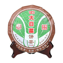 Load image into Gallery viewer, Chinese tea cake with green leaf design in brown wrapper on wooden stand, Puerh Da Bai Cai