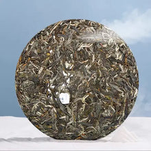 Carica l'immagine nel visualizzatore di Gallery, Round compressed Chinese pu-erh tea cake with visible tea leaves, displayed on a white cloth background.