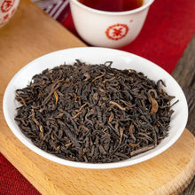 Cargar imagen en el visor de la galería, Loose leaf Chinese black tea in a white bowl beside a cup of brewed tea on a wooden board
