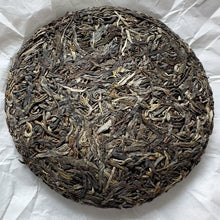 Load image into Gallery viewer, Compressed Chinese raw pu-erh tea cake with dried whole tea leaves on white paper
