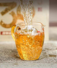 Load image into Gallery viewer, Freshly brewed Chinese tea being poured into a clear glass pitcher, amber color, bubbles rising.
