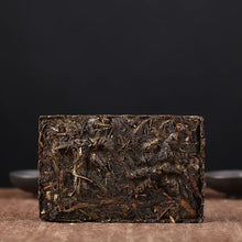 Load image into Gallery viewer, Compressed puerh tea brick on brown fabric with dark background