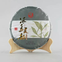 Load image into Gallery viewer, Chinese puerh tea cake with leaf design, wrapped, on a wooden stand