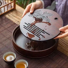 Load image into Gallery viewer, Person holding a wooden tea tray with artistic design on a wooden   Product Name: Round Tea Tray

Material: Bamboo + Laminate Board Base

Size:

Small : Diameter 25 * Height 5 cm

Medium: Diameter 29 * Height 5 cm

Large : Diameter 38 * Height 5 cm



This Round Tea Tray is an exquisite piece of craftsmanship, designed for the ritual of Gongfu tea, a traditional Chinese method of tea preparation that focuses on the aesthetic presentation and sharing. The tray is constructed from high-quality bamboo, atable.