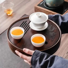 Load image into Gallery viewer, Tea set with three white cups and a white teapot on a wooden tray, held by a person. Product Name: Round Tea Tray

Material: Bamboo + Laminate Board Base

Size:

Small : Diameter 25 * Height 5 cm

Medium: Diameter 29 * Height 5 cm

Large : Diameter 38 * Height 5 cm



This Round Tea Tray is an exquisite piece of craftsmanship, designed for the ritual of Gongfu tea, a traditional Chinese method of tea preparation that focuses on the aesthetic presentation and sharing. The tray is constructed from high-qualit