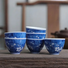 Load image into Gallery viewer, Set of blue porcelain Chinese tea cups with white plum blossom design on wooden table