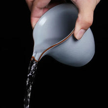 Load image into Gallery viewer, Hand pouring water from a ceramic gaiwan fairness pitcher against black background