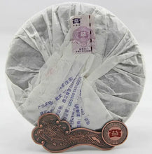 Load image into Gallery viewer, Wrapped puerh tea cake with Chinese label on a decorative metal tea stand