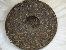 Load image into Gallery viewer, Compressed Sheng Puerh tea cake with visible tea leaves on white wrapping paper.