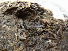 Load image into Gallery viewer, Close-up of compressed puerh tea cake, showing dried tea leaves and textured surface.