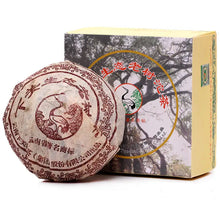 Load image into Gallery viewer, Chinese Pu-erh tea cake with printed wrapper beside a decorative box featuring tree artwork