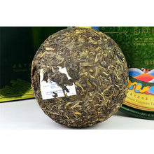 Load image into Gallery viewer, Compressed Chinese puerh tea cake with loose tea leaves and paper label, displayed on table.