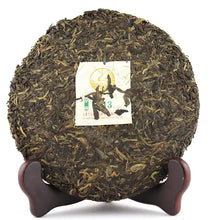 Load image into Gallery viewer, Compressed raw puerh tea cake with Chinese label on wooden stand