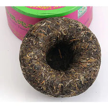 Charger l'image dans la galerie, Compressed sheng puerh tea cake with loose leaf texture and round hole center, in front of tin container