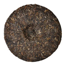 Load image into Gallery viewer, Compressed round puerh tea cake with visible loose tea leaves on white background