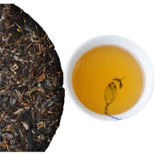 Load image into Gallery viewer, Compressed puerh tea cake next to a cup of golden brewed Chinese tea