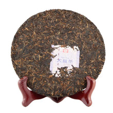 Load image into Gallery viewer, Pressed Pu-erh tea cake on wooden stand with visible tea leaves and center label