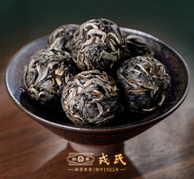Load image into Gallery viewer, Bowl of Chinese Puerh tea balls with dry loose leaf texture on a wooden table