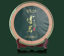 Load image into Gallery viewer, Chinese Pu-erh tea cake with gold Chinese characters, wrapped in paper, displayed on a wooden stand.