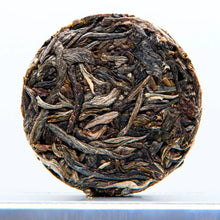 Load image into Gallery viewer, Compressed round cake of loose leaf raw puerh tea with visible whole tea leaves.