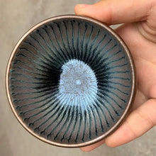Load image into Gallery viewer, Hand holding a Jian Zhan style ceramic tea cup with blue crystalline glaze and radial pattern