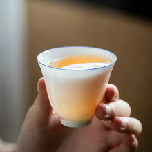 Load image into Gallery viewer, Hand holding a white porcelain gongfu tea cup with light amber Chinese tea
